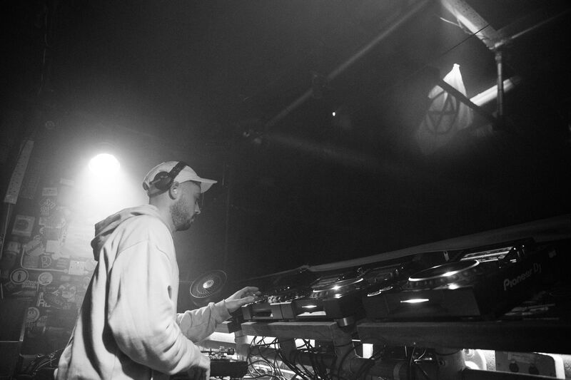 Black-and-white photo of Theon Bower in a cap and hoodie mixing on CDJs