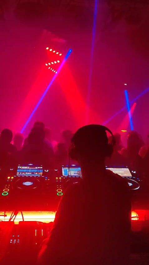 Theon Bower in headphones at the decks under red and blue lasers