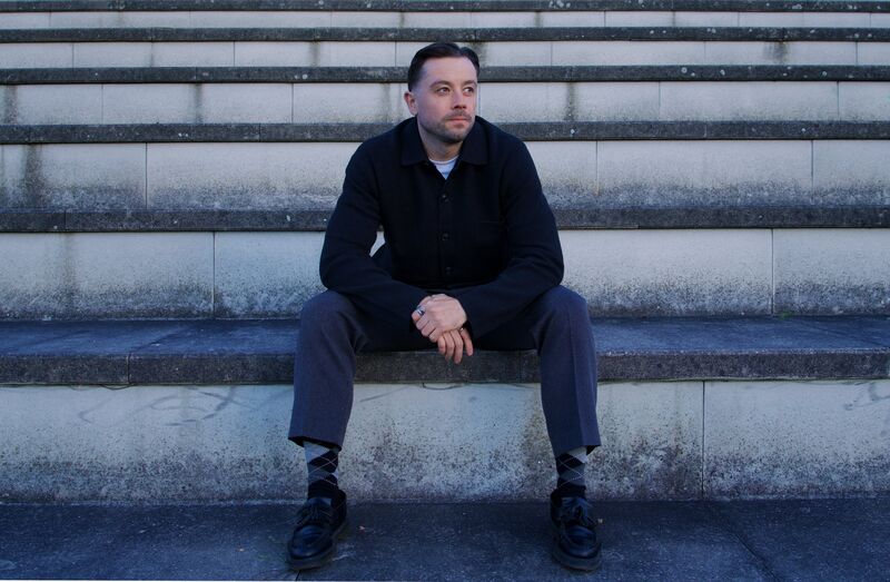 Theon Bower sitting on stone steps in Berlin, looking to the side